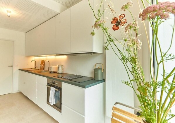 A modern kitchen with white cabinets, a green countertop, and a built-in oven. There is a window with a view of greenery outside. - La Quinta Bordeaux-Bègles (Bègles)