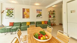 Un salon moderne avec un canapé vert, une table à manger en bois sur laquelle est posé un panier de fruits, et un plafond doté d’un éclairage encastré.