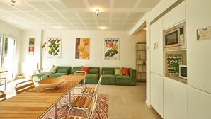 Un salon moderne avec une table à manger en bois, des canapés verts et un coin cuisine équipé d’un four à micro-ondes.