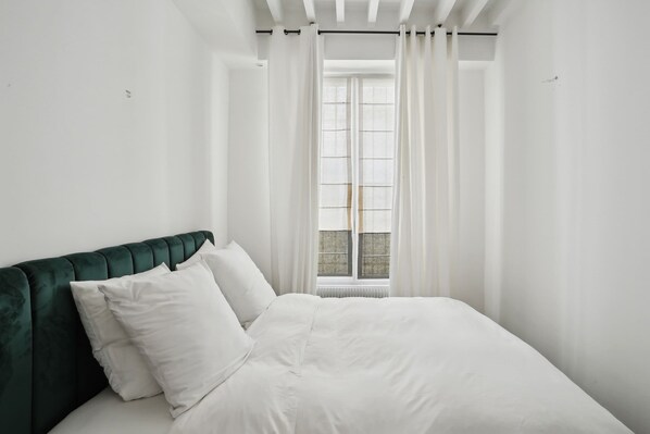 A bedroom with a bed, white curtains, and a window with blinds. - Spacious 2BR in The Heart of Saint Germain (Paris)