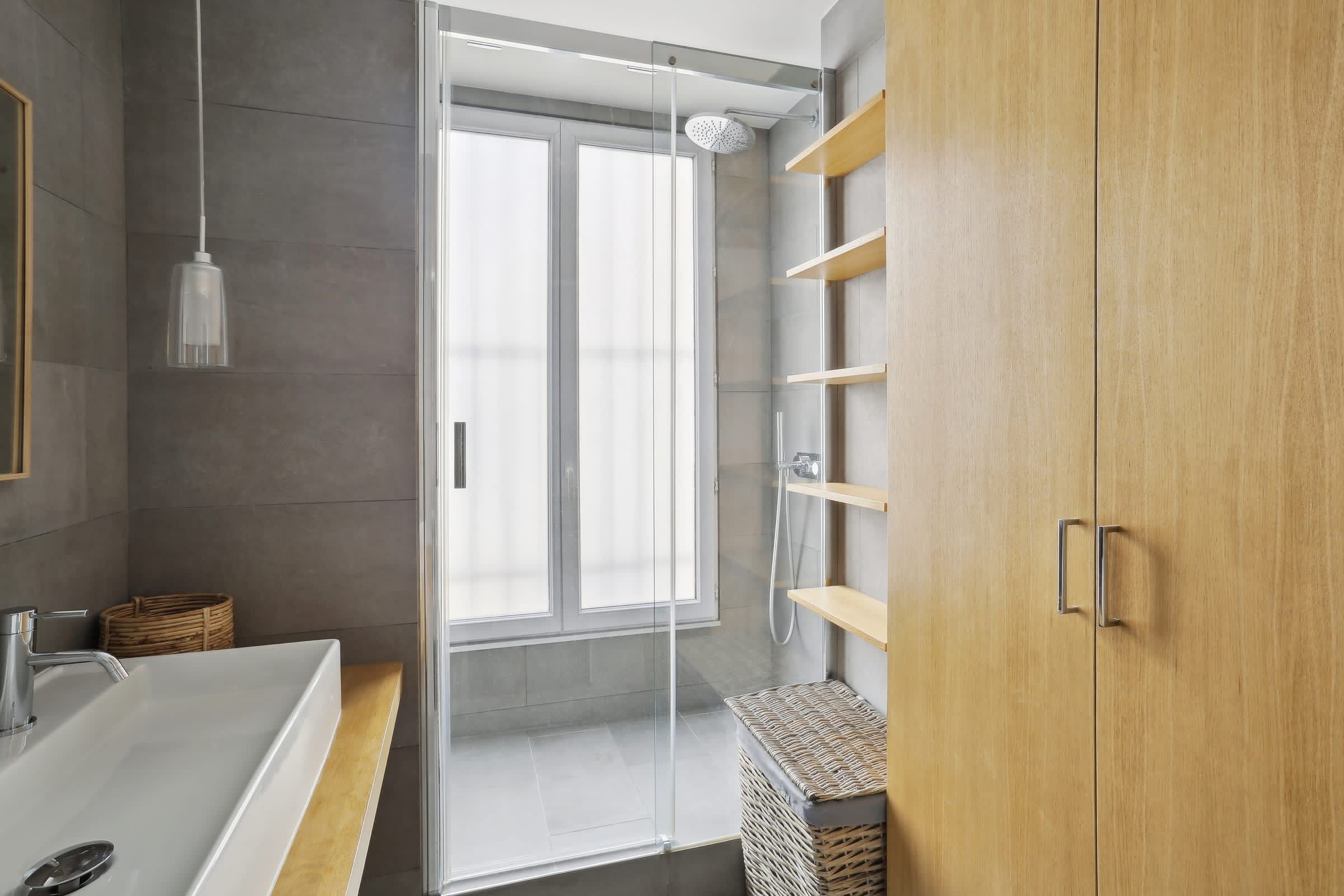 A modern bathroom with a glass shower enclosure, a white sink, and wooden shelves.