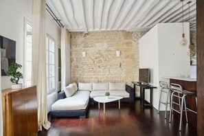 A modern living room with a stone wall, a sofa, a coffee table, and a bar area. - Spacious 2BR in The Heart of Saint Germain (Paris)