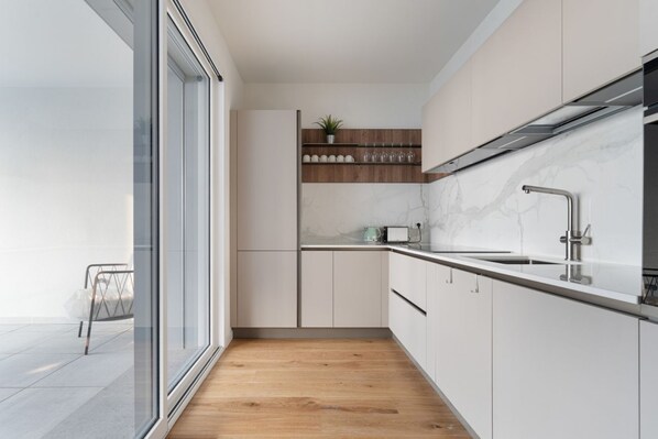 Una cocina moderna con armarios blancos, suelo de madera, salpicadero de mármol y grifo de acero inoxidable.
