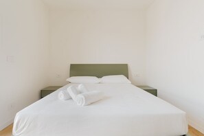 Una cama individual con cabecera verde, ropa de cama blanca y dos toallas enrolladas en el reposapiés.