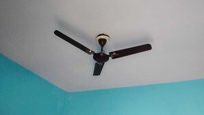 A ceiling fan with three blades in a room with blue walls. - Hotel Shri Ganesh Hari Ganesh (Ukhimath)