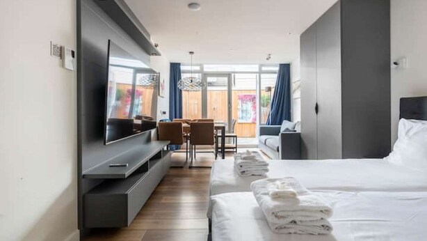 Ein modernes Hotelzimmer mit einem großen Bett, einem an der Wand befestigten Fernseher, einem Schreibtisch mit Stuhl und einem Balkon mit Vorhängen.