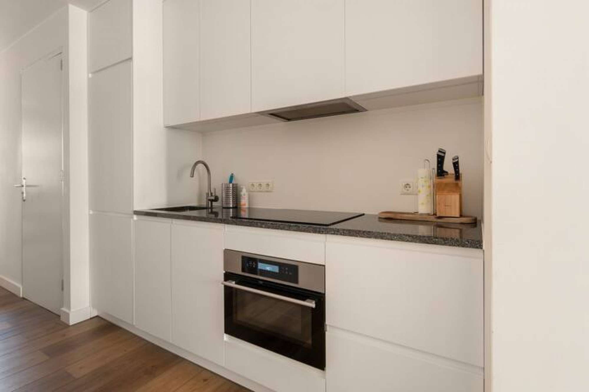 A modern kitchen with white cabinetry, a stainless steel oven, a black countertop, and a built-in microwave.