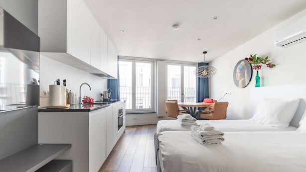 Una camera d'albergo moderna con angolo cottura, zona pranzo e un letto con asciugamani ordinatamente piegati.