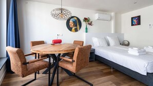 Una camera d'albergo moderna con un tavolo rotondo in legno, sedie imbottite marroni, un letto con lenzuola bianche e un condizionatore d'aria a parete.