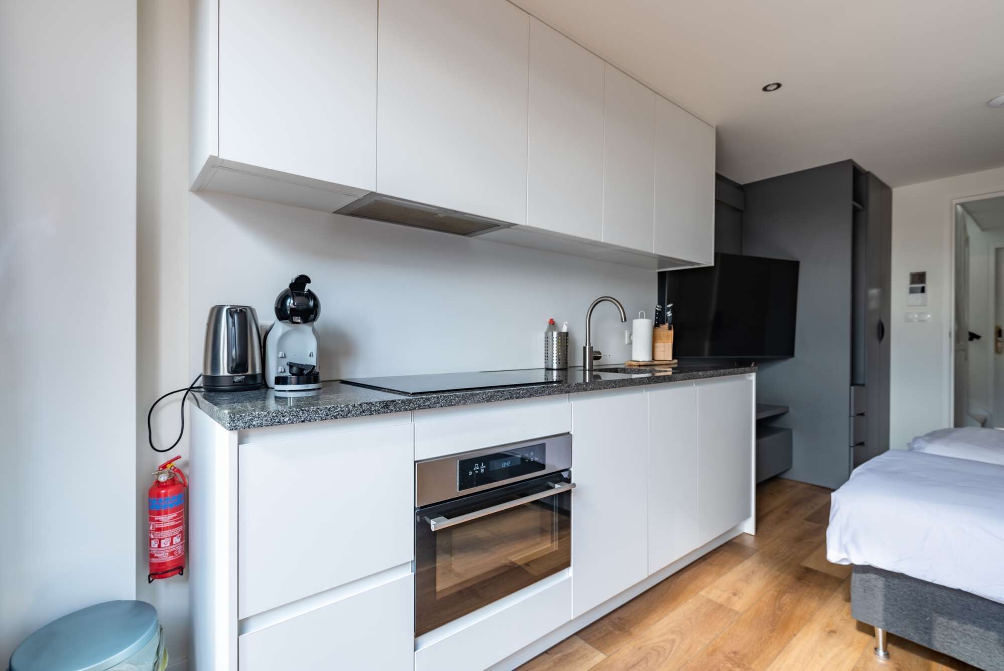 Een moderne keuken met witte kasten, een ingebouwde oven, een koffiezetapparaat en een televisie boven de aanrecht.