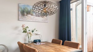 Et spiseområde med et træbord, læderstole i brunt, en dekorativ lysekrone, en vase med blomster og et maleri på væggen.