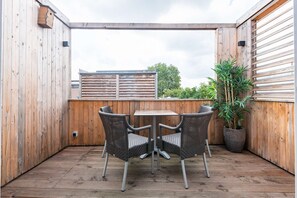 A wooden deck with a table and two wicker chairs, a potted plant, and a wooden fence. - Stylish studio with terrace in the heart of Breda city center (Breda)