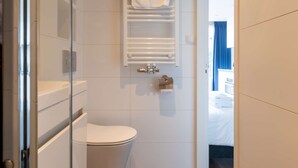 Et moderne badeværelse med toilet, glasvæg omkring brusebad og en hvid vask.