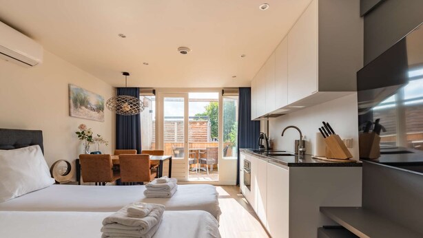Et moderne hotelværelse med to senge, et tekøkken og en balkon med træterrasse.