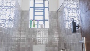 A bathroom with tiled walls, a window, a showerhead, and a toilet.