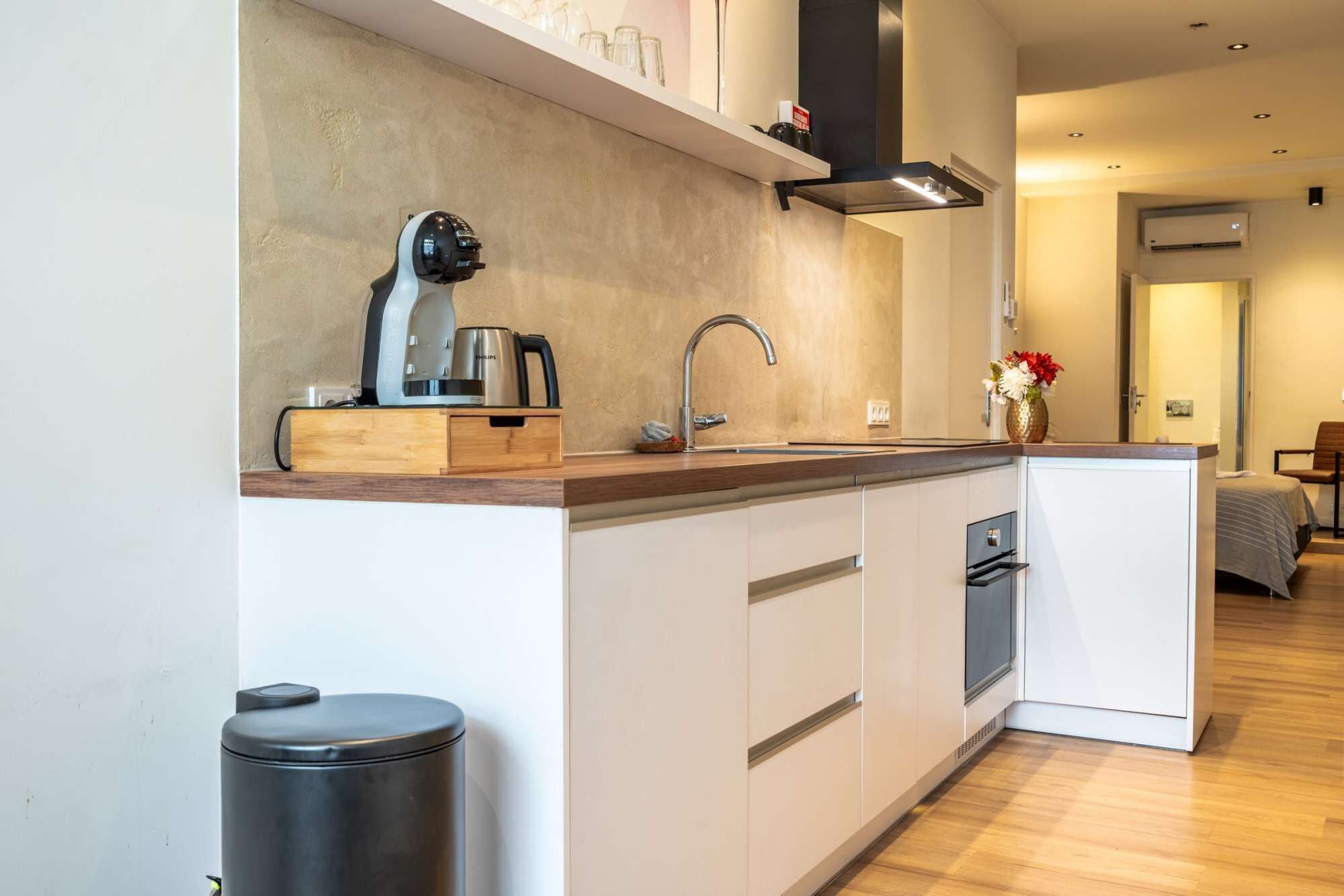 A compact kitchen with a modern design, featuring a built-in dishwasher, a coffee maker, and a trash bin.