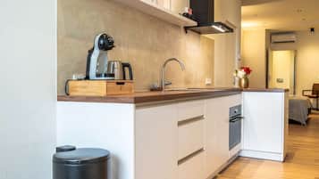 A compact kitchen with a modern design, featuring a built-in dishwasher, a coffee maker, and a trash bin.