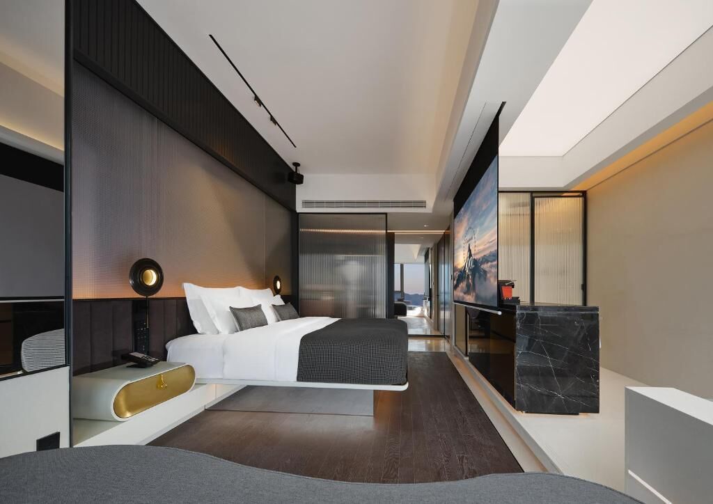 A modern hotel room with a large bed, a desk, and a view of the cityscape.