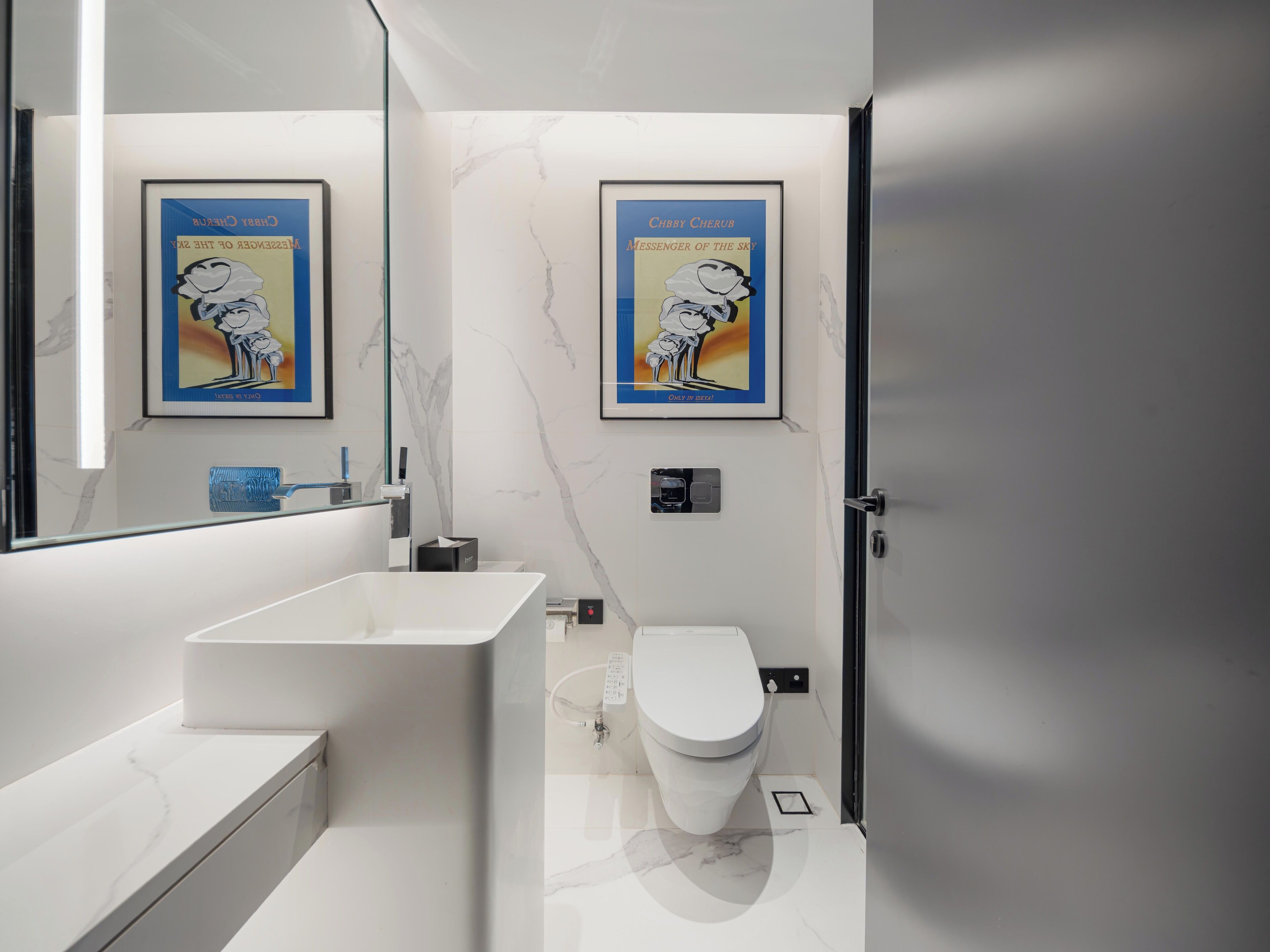 Un baño moderno con un lavabo blanco, inodoro y paredes de mármol. Hay dos carteles enmarcados en la pared.