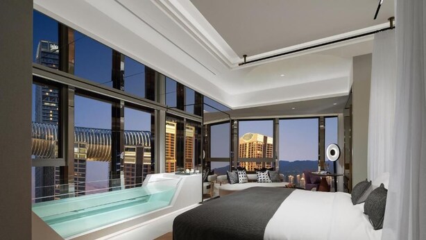 Une chambre d’hôtel moderne dotée d’un grand lit, d’un jacuzzi entouré de parois de verre et offrant une vue sur la ville.