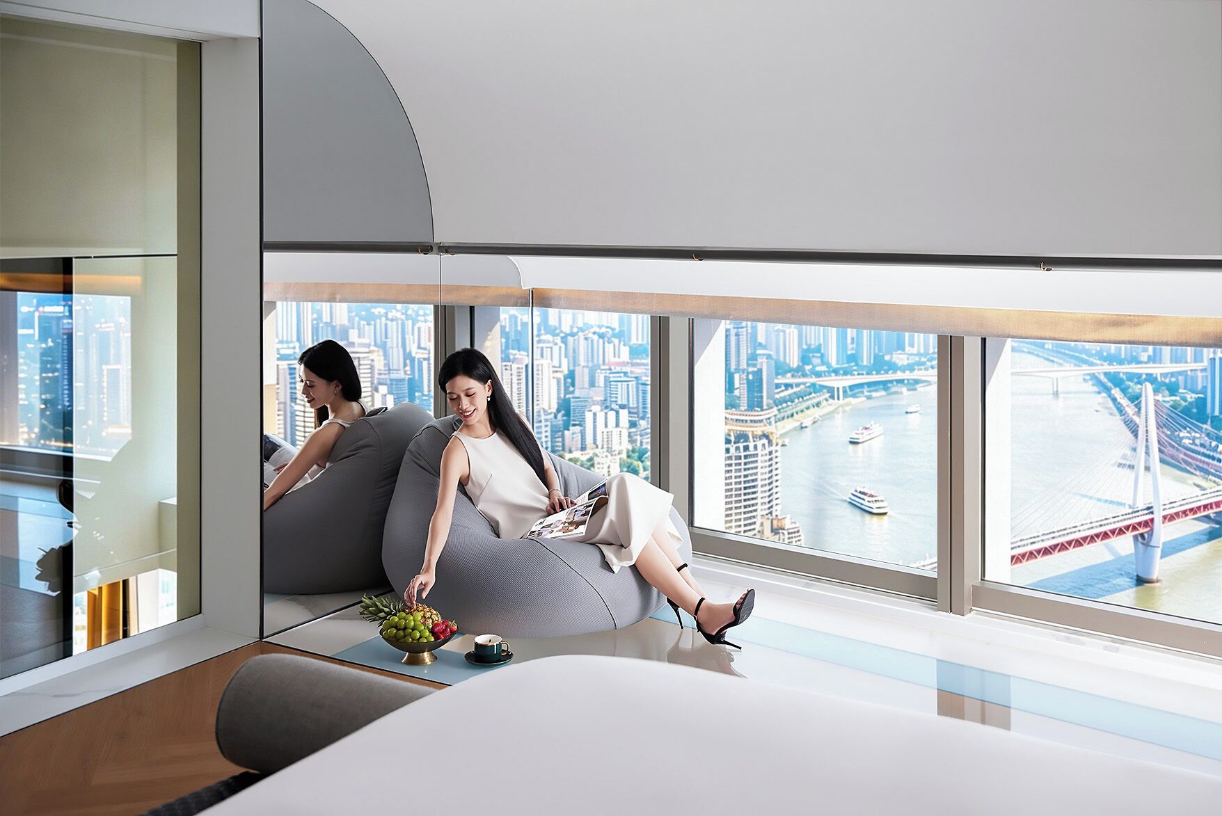 A modern interior with a large window overlooking a cityscape, a sofa, and a small table with fruits and a cup.