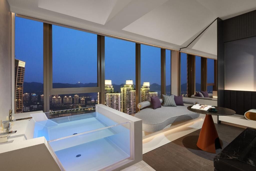 A modern hotel room with a large bathtub, a sofa, and a dining table.