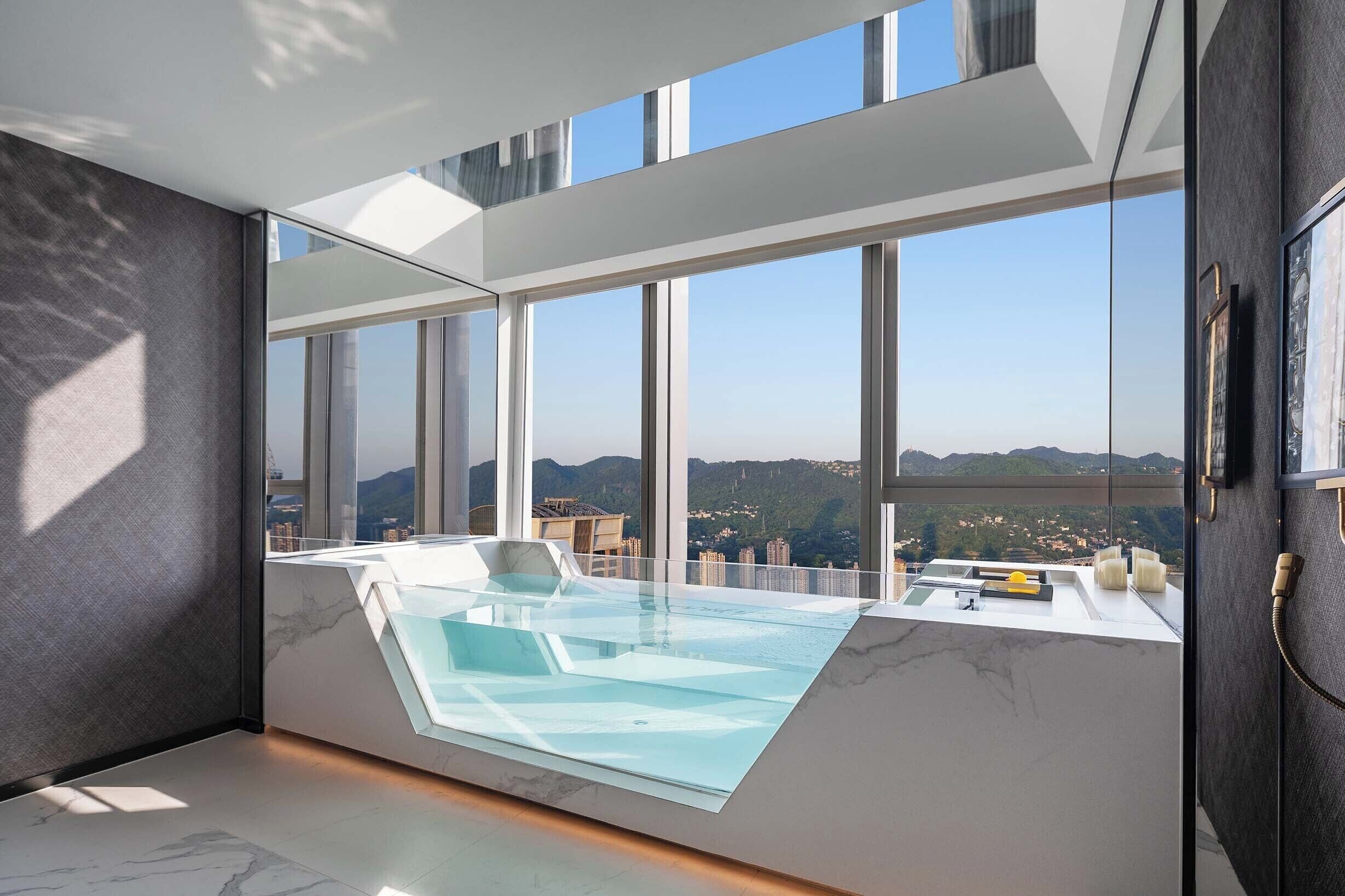 Una habitación moderna con piscina de fondo de cristal, ventanas amplias y vistas a un paisaje urbano.