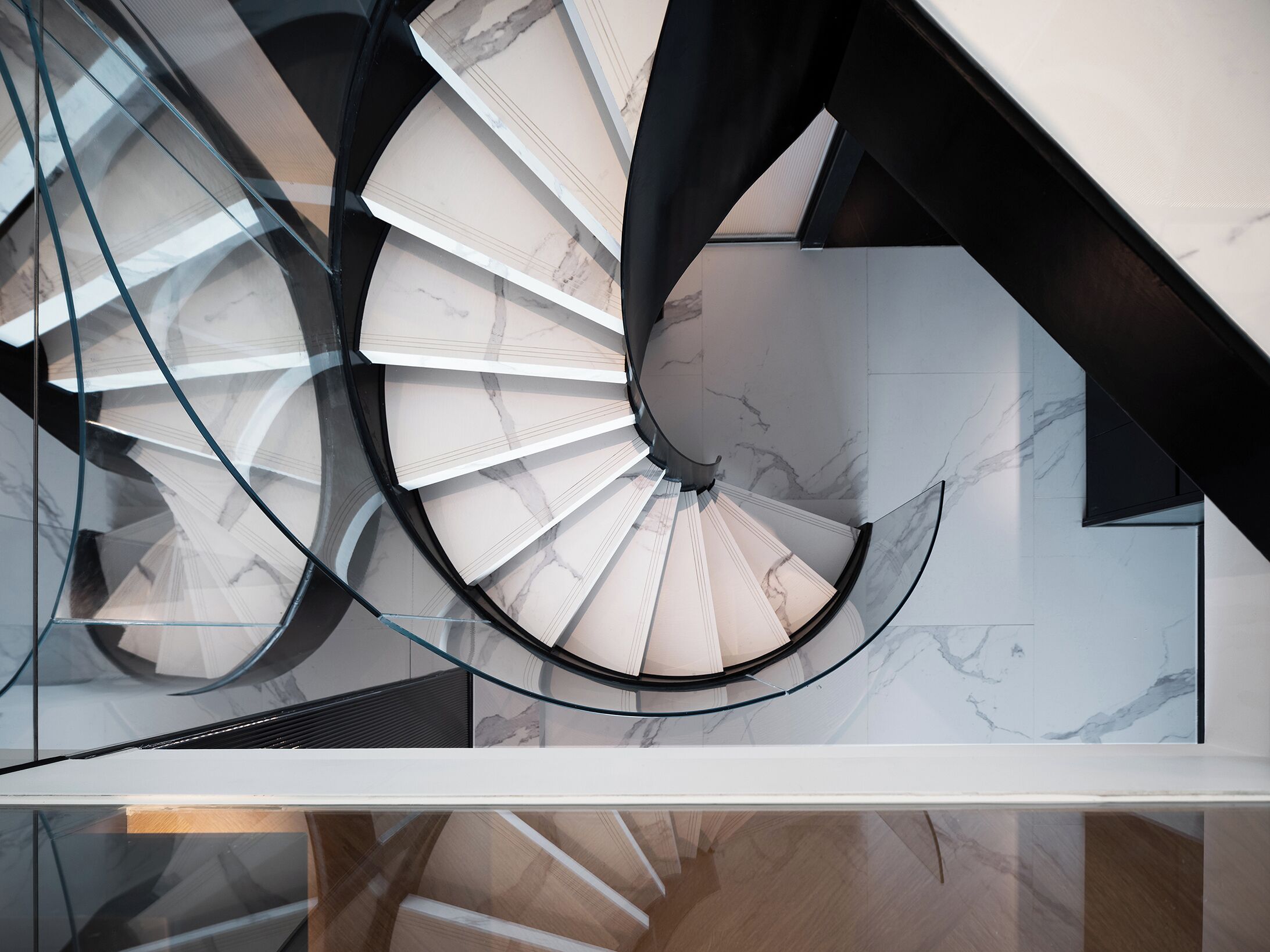 A spiral staircase with marble steps and glass railings.