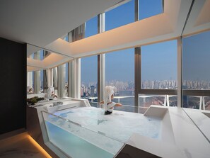 Hotelkamer hoog in een wolkenkrabber met een groot raam, een klein binnenzwembad en uitzicht over de stad.
