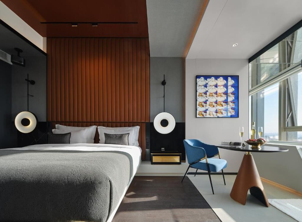 Ein modernes Hotelzimmer mit einem großen Bett, einem kleinen Tisch mit Stuhl und einem großen Fenster.