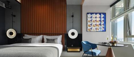 Ein modernes Hotelzimmer mit einem großen Bett, einem kleinen Tisch mit Stuhl und einem großen Fenster.