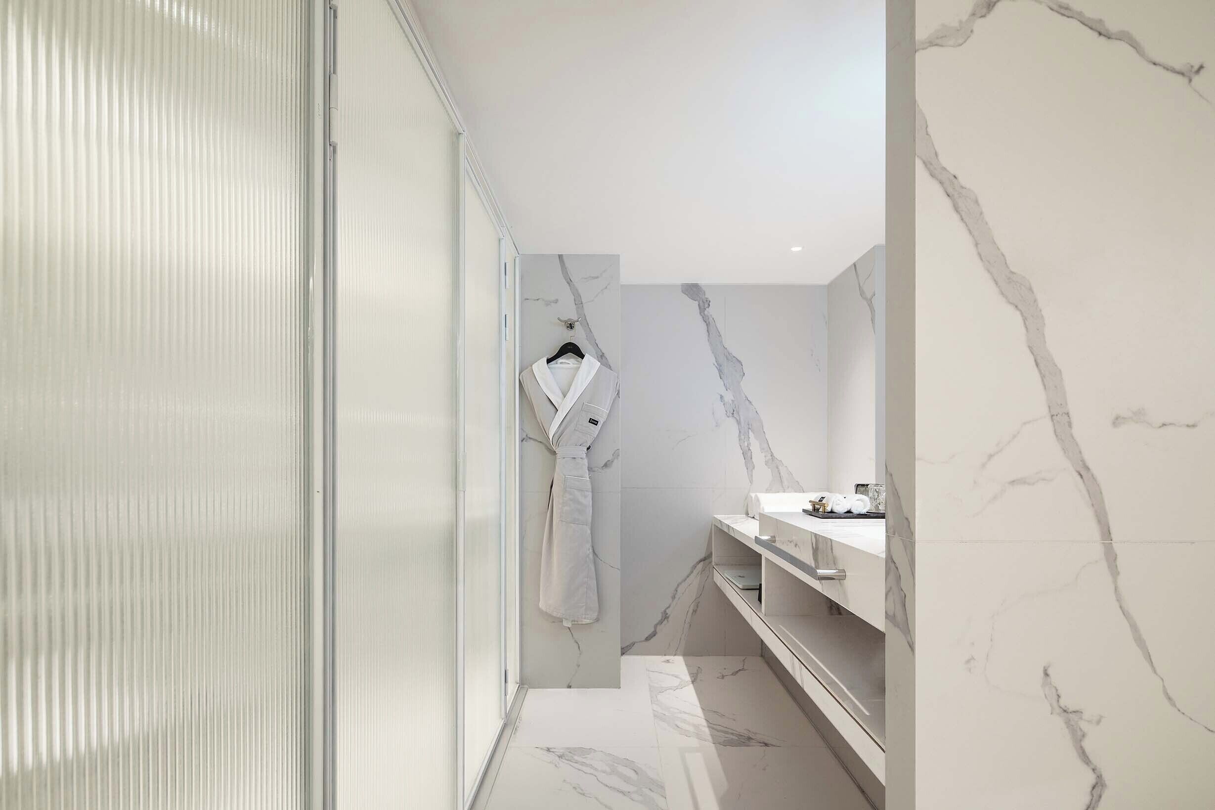 Un baño moderno con pared de mármol, una bata colgada en un perchero y un tocador con espejo.
