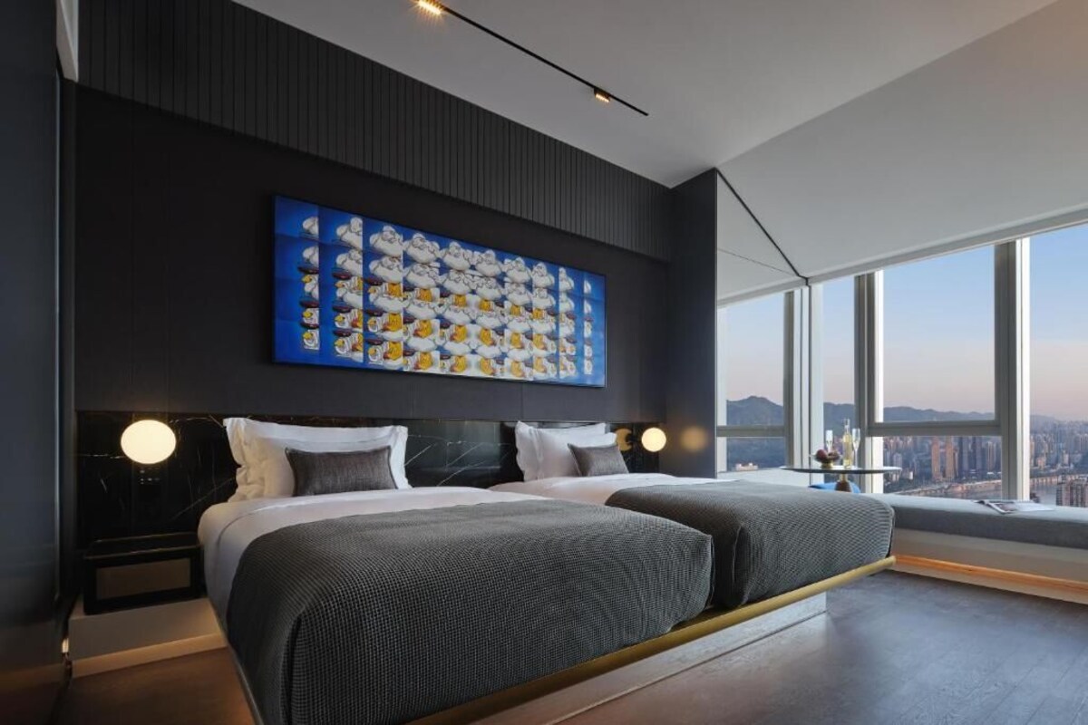 Een moderne hotelkamer met een uitgebreid stadsgezicht, een groot abstract schilderij aan de muur en een bed met hoofdeinde.