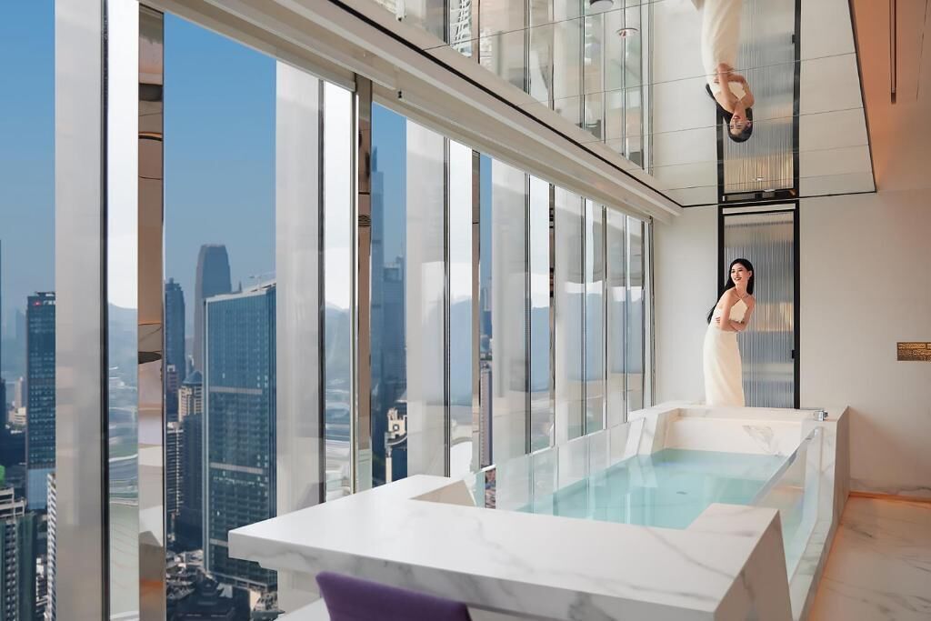 Une chambre d’hôtel située dans un immeuble de grande hauteur, dotée d’une grande fenêtre en verre, d’une baignoire en marbre et offrant une vue sur la ville.