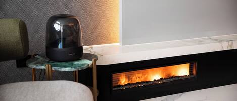 A modern living room with a fireplace, a mounted television, and a small table with a speaker.