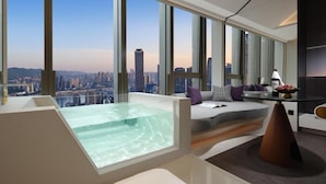 Ein modernes Hotelzimmer mit weitreichendem Stadtblick, einer Glaskuppel-Hottube und einer gemütlichen Sitzecke mit Tisch und Stühlen.