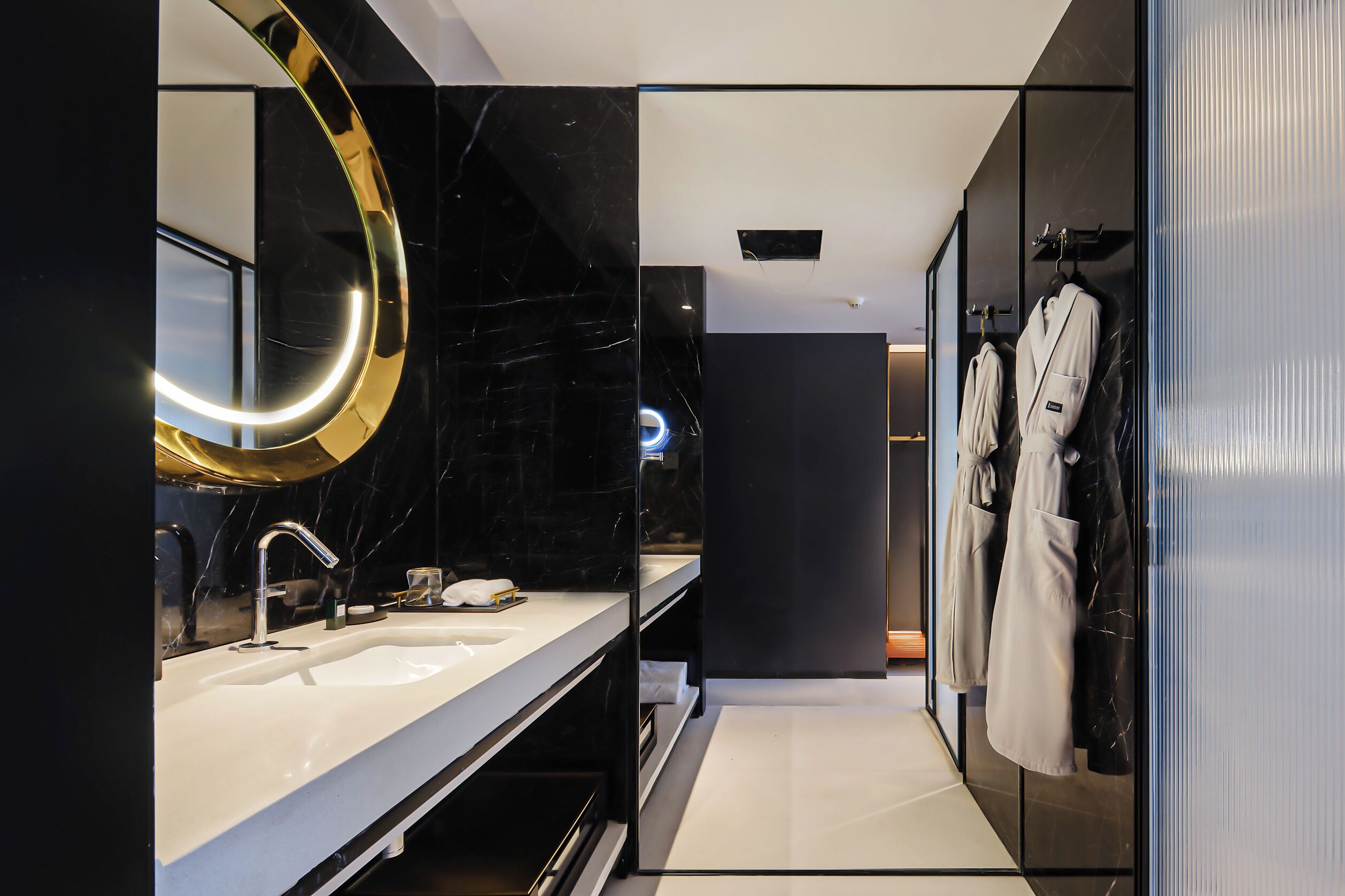 A modern bathroom with a large mirror, a sink, and a robe rack.