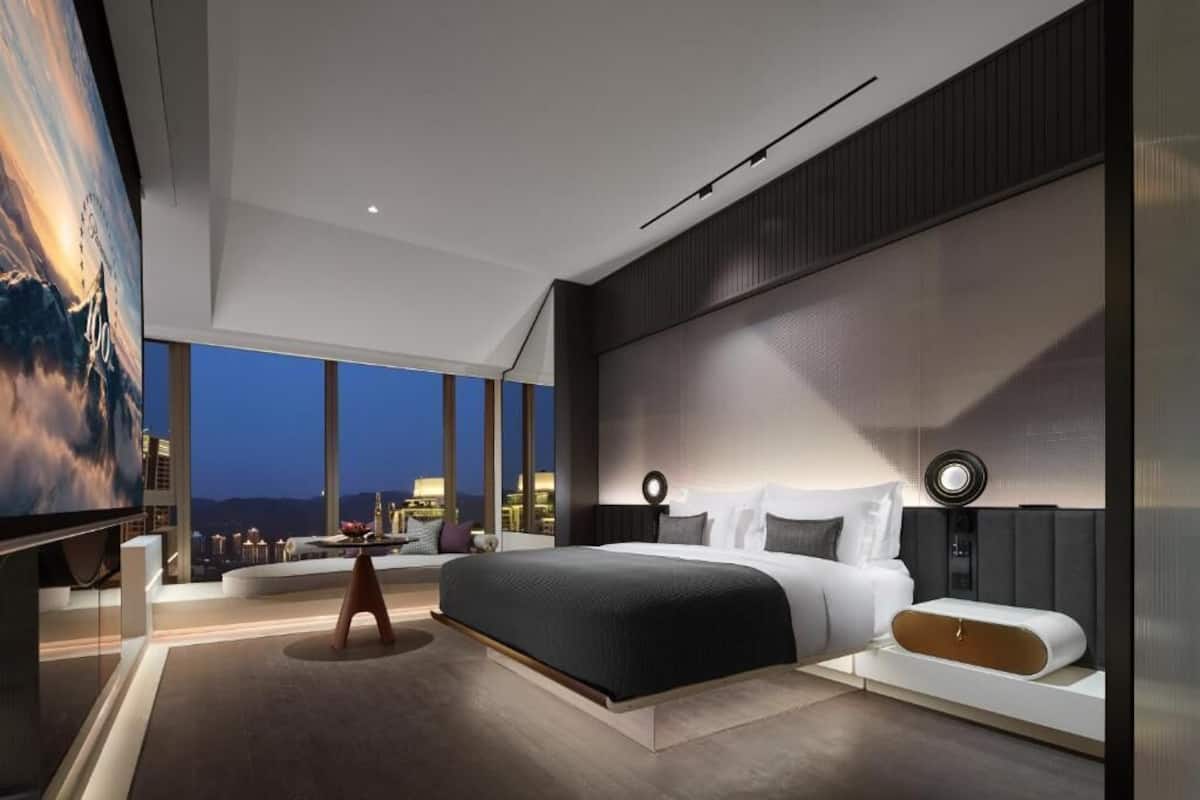 Ein modernes Schlafzimmer mit einem großen Bett, einem Fernseher und Blick auf die Stadt.