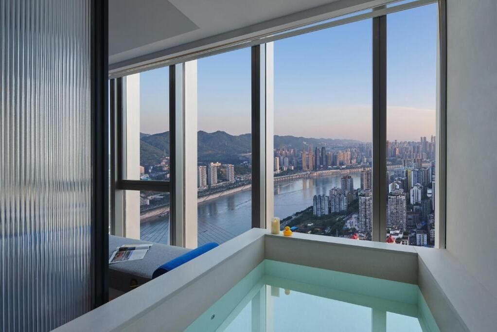 Ein modernes Zimmer mit großem Fenster und Blick auf die Stadt, einer kleinen Badewanne und einer Sitzecke.
