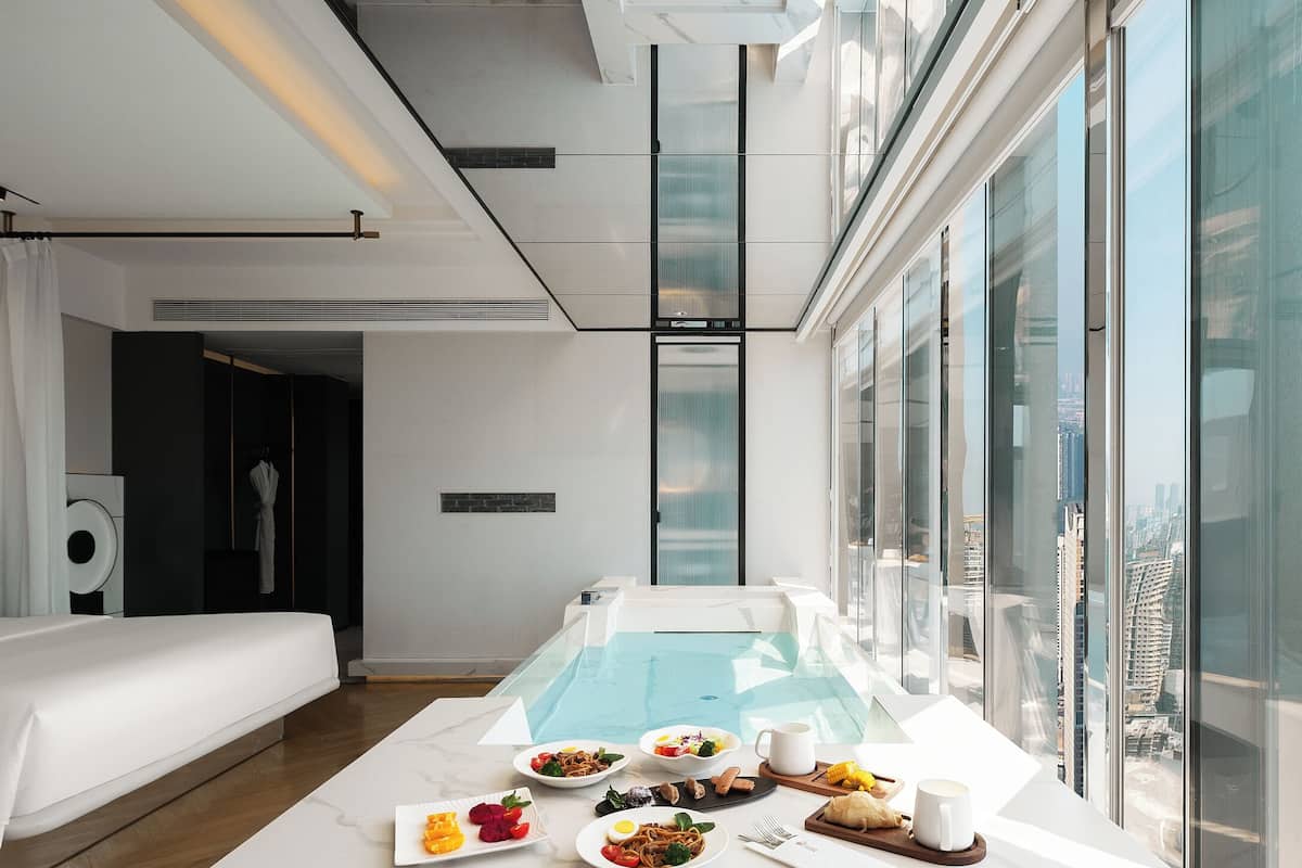 Ein modernes Hotelzimmer mit großem Fenster, einem Billardtisch und einem Essbereich mit Frühstück.