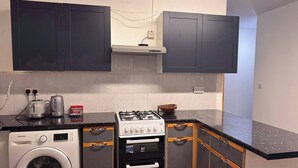 A compact kitchen with a washing machine, a gas stove, and a microwave. - Modern Nextdoor Stays (Morden)
