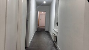 A narrow hallway with white walls, a grey carpet, and a ceiling light. - Modern Nextdoor Stays (Morden)