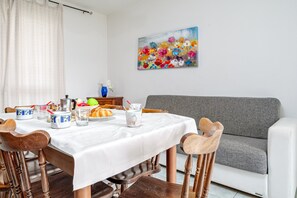 Un coin repas avec une table mise pour le petit-déjeuner, un canapé gris et un tableau coloré accroché au mur.