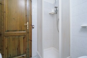 Ein Badezimmer mit Holztür, weißen Fliesenwänden, einer Dusche und einer Toilette.