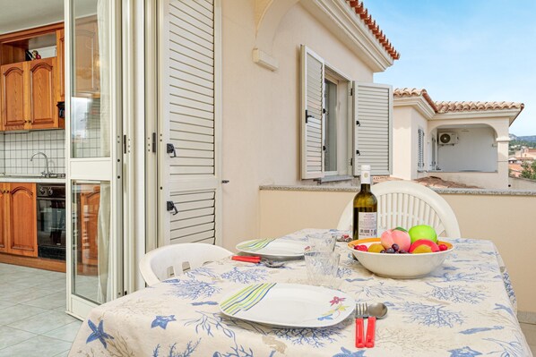 Une table à manger avec un saladier de fruits, une bouteille et des couverts, le tout posé sur une nappe à motifs.