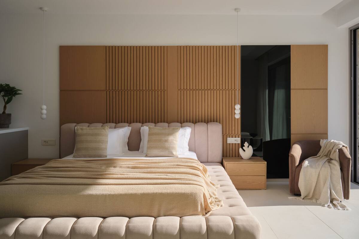 A modern bedroom with a large bed, a wooden headboard, bedside tables, and a chair.
