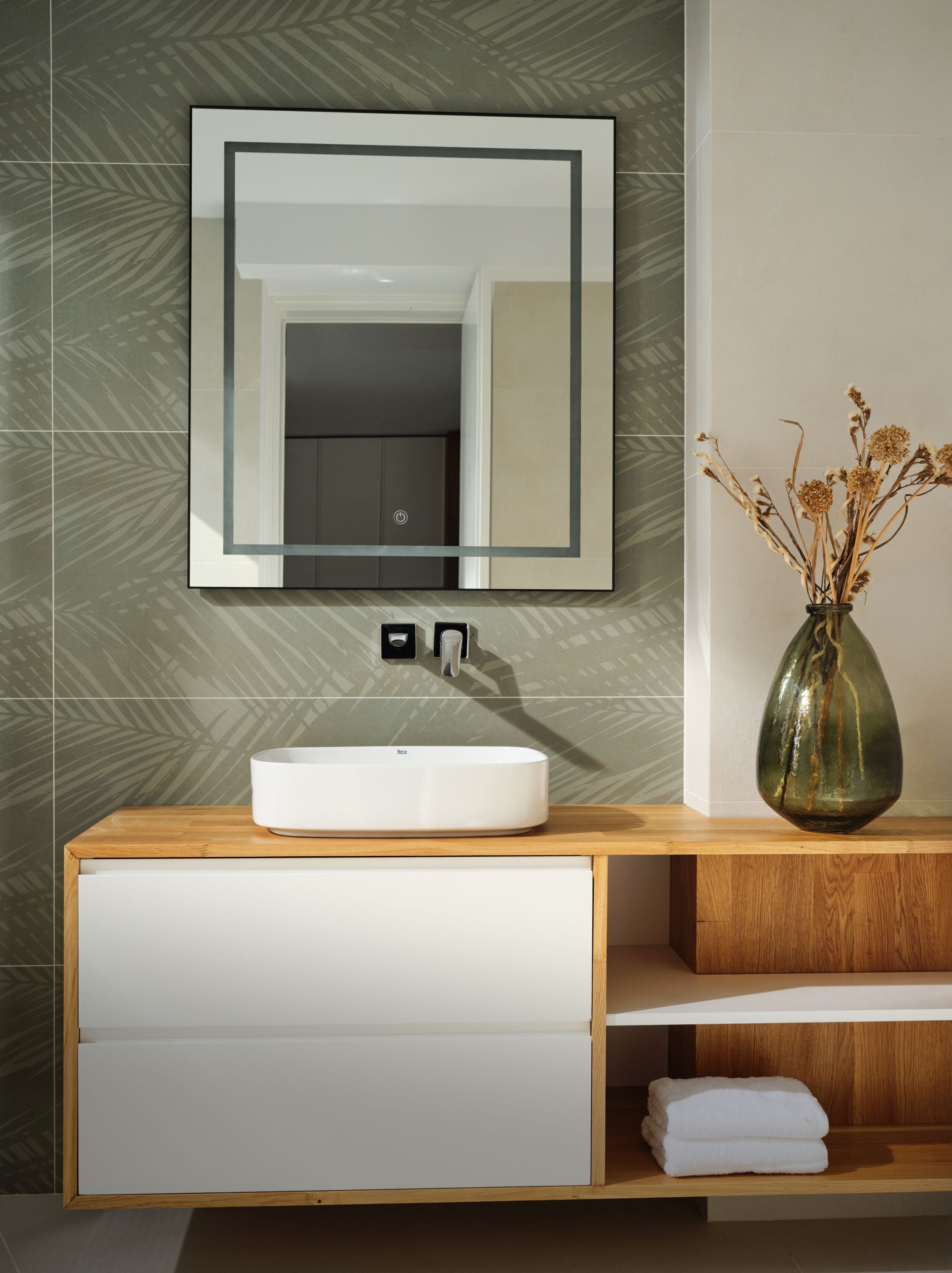 A bathroom with a white sink, a mirror, a vase with dried flowers, and a towel on a wooden shelf.