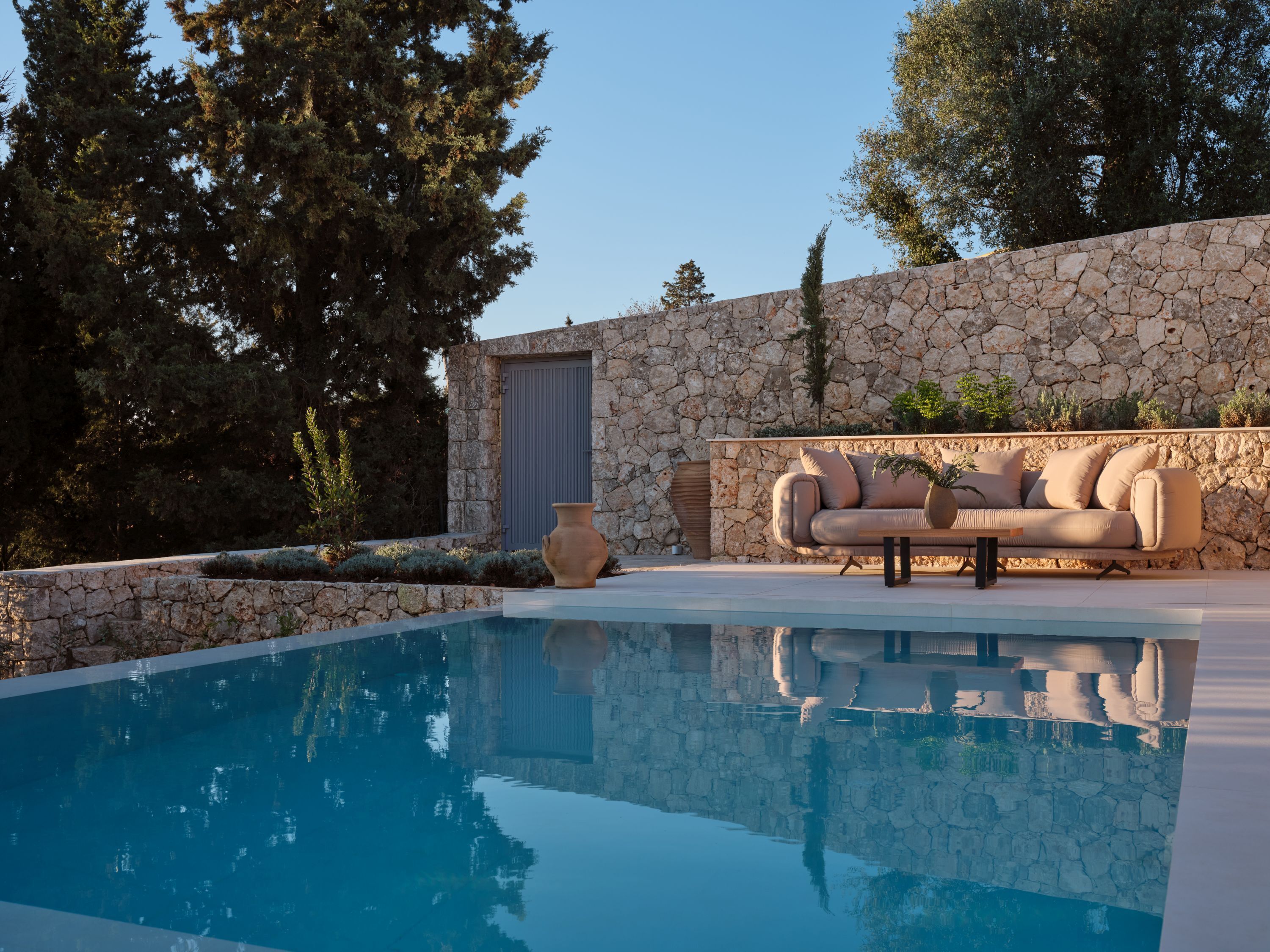 A pool with a stone wall, a beige sofa, and a potted plant.