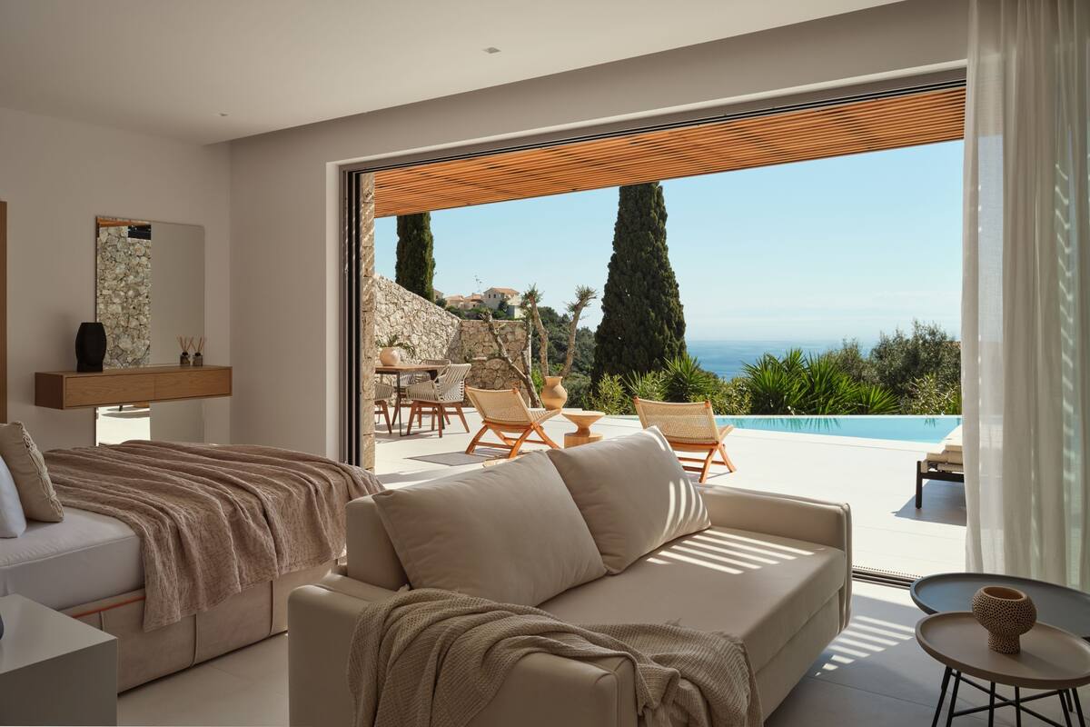 A modern bedroom with a large bed, a sofa, and a view of the sea.
