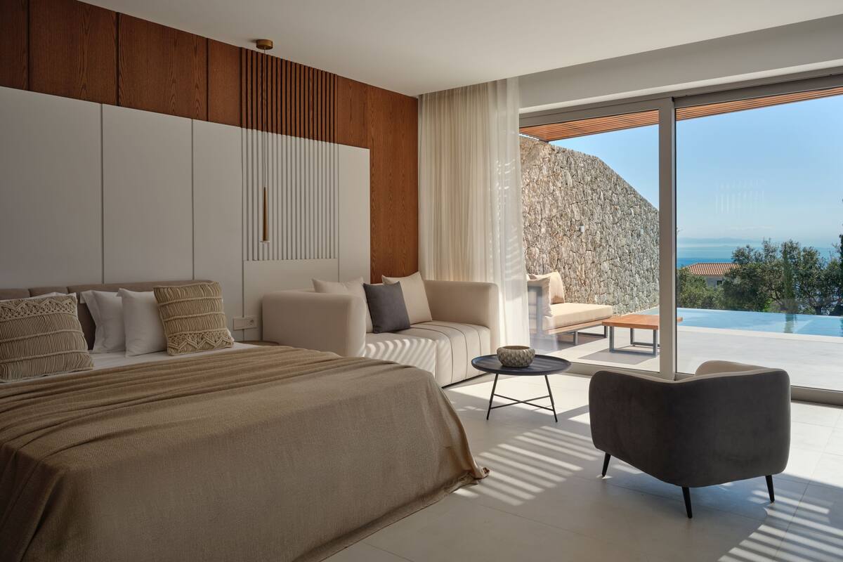 A modern bedroom with a large bed, a sofa, a coffee table, and a view of the ocean.